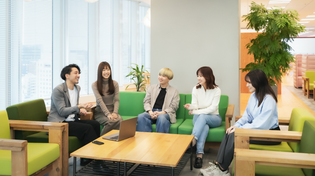 The spacious office room is furnished with a variety of desk and chair designs. Natural light pours in, accented by houseplants.